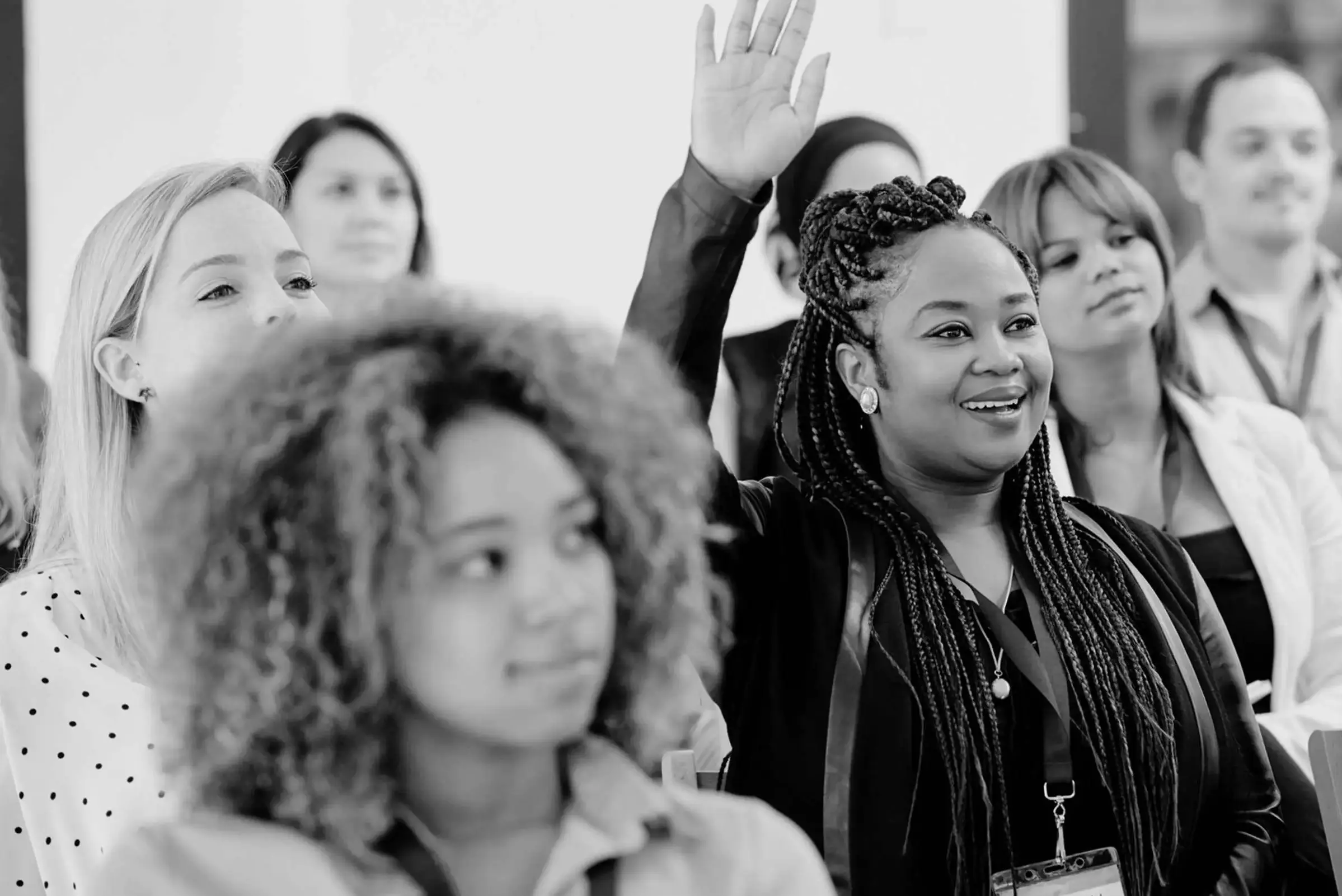 Smiling woman raising her hand during a conference session, surrounded by attentive attendees.